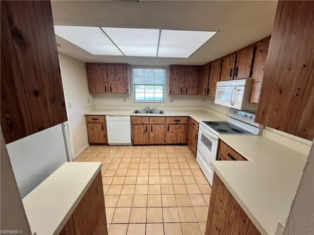 Kitchen with white appliances, light countertops, light tile patterned flooring, and brown cabinetry