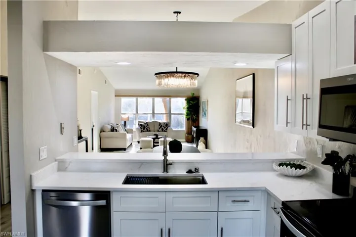 Kitchen with open floor plan, stainless steel appliances, white cabinets, light stone countertops, and a chandelier