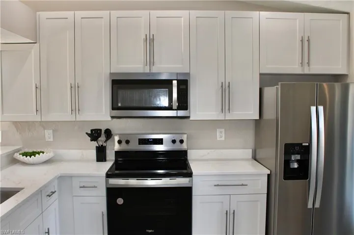 Kitchen with appliances with stainless steel finishes, white cabinetry, and light stone countertops