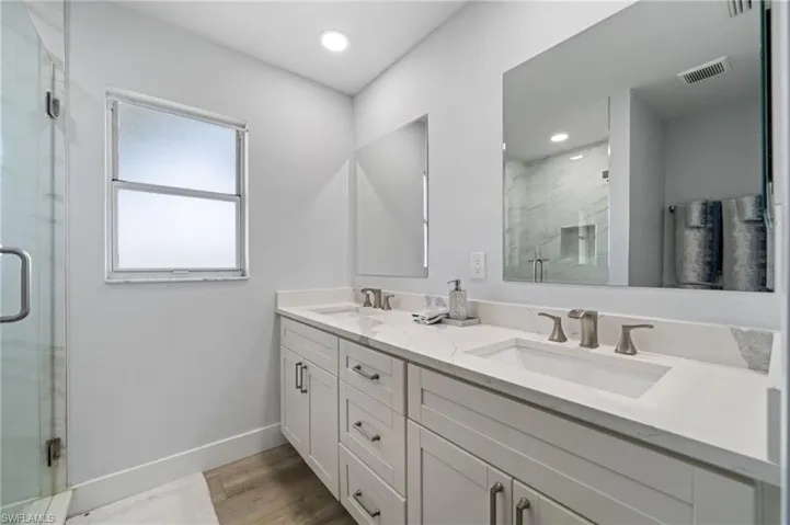 Full bath with double vanity, a marble finish shower, light wood-type flooring, and recessed lighting