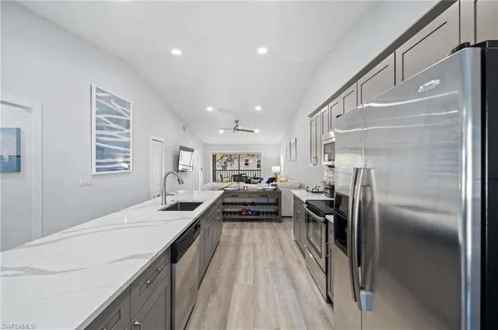 Kitchen featuring stainless steel appliances, gray cabinets, lofted ceiling, open floor plan, and light wood finished floors