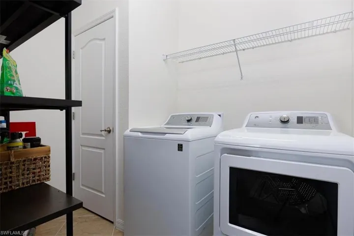 Washroom with washing machine and dryer and light tile patterned flooring