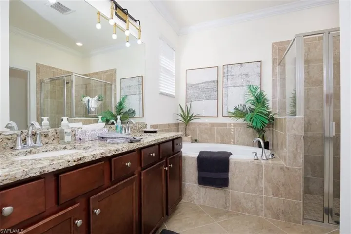 Full bathroom with double vanity, a garden tub, ornamental molding, a stall shower, and light tile patterned floors