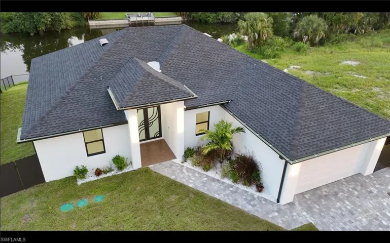 View of front of house featuring a front yard, stucco siding, a water view, a garage, and a shingled roof