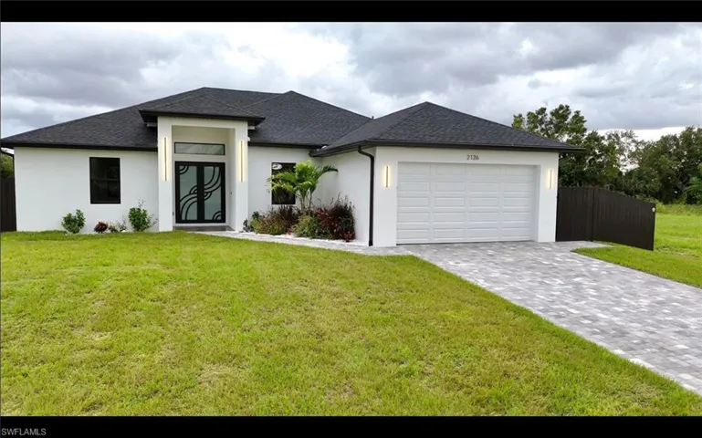 View of front facade featuring stucco siding, roof with shingles, decorative driveway, and an attached garage