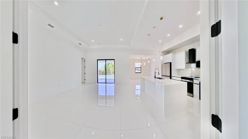 Kitchen with white cabinetry, open floor plan, a tray ceiling, hanging light fixtures, and a kitchen island with sink