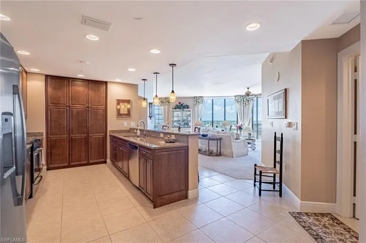 Kitchen with appliances with stainless steel finishes, sink, light stone counters, pendant lighting, and light tile patterned floors