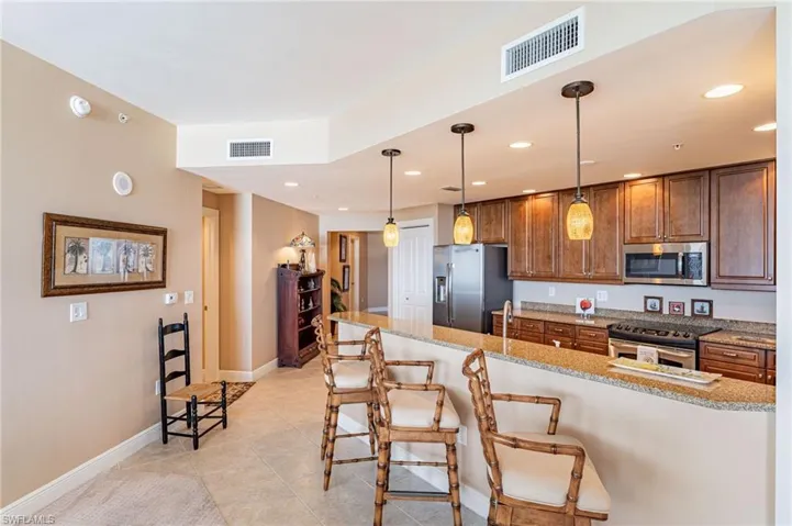 Kitchen with light tile patterned flooring, hanging light fixtures, light stone countertops, appliances with stainless steel finishes, and a kitchen breakfast bar