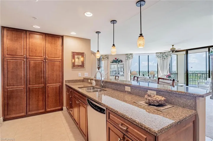 Kitchen featuring light tile patterned flooring, dishwasher, light stone counters, decorative light fixtures, and sink