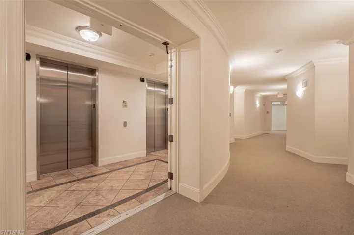 Hall with light colored carpet, elevator, and ornamental molding