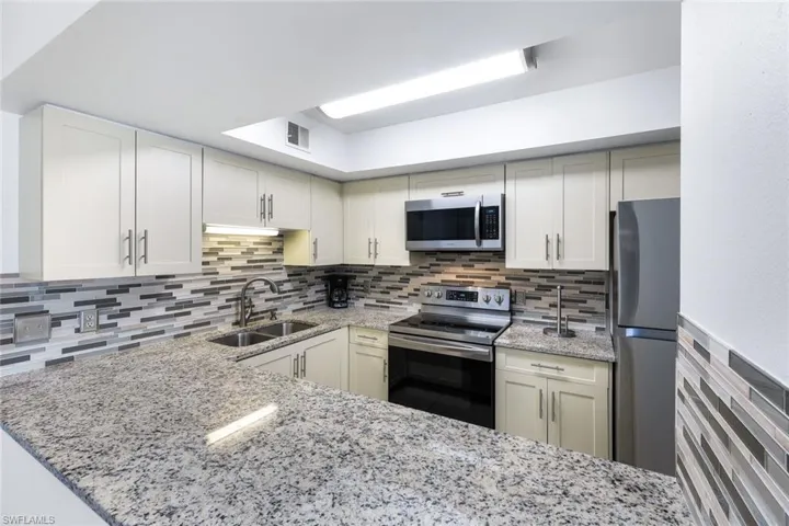 Kitchen featuring stainless steel appliances, light stone counters, tasteful backsplash, and sink