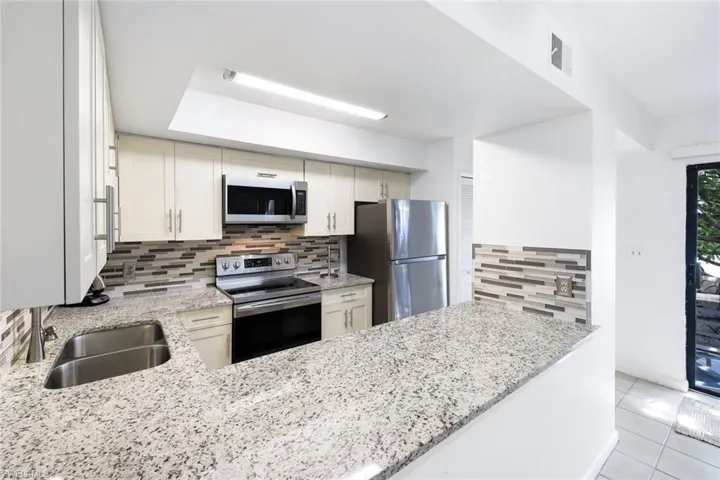 Kitchen featuring stainless steel appliances, backsplash, and light stone counters