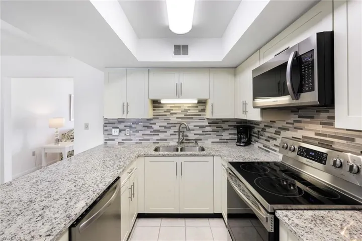 Kitchen with sink, appliances with stainless steel finishes, light stone countertops, and decorative backsplash