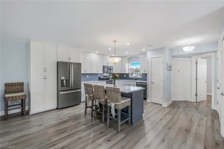 Kitchen featuring white cabinetry, decorative light fixtures, a center island, appliances with stainless steel finishes, and light hardwood / wood-style flooring