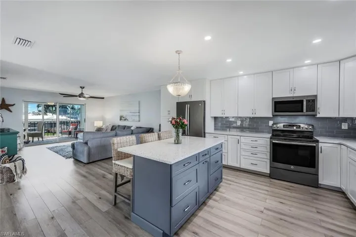 Kitchen featuring appliances with stainless steel finishes, white cabinets, pendant lighting, backsplash, and light hardwood / wood-style floors