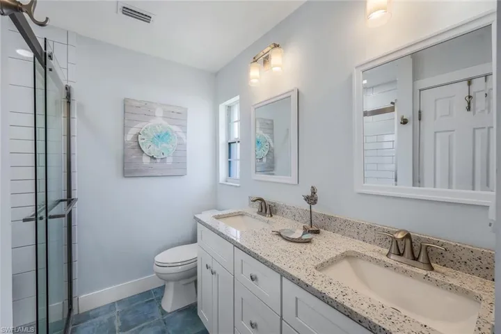 Bathroom featuring tile patterned flooring, walk in shower, double sink vanity, and toilet