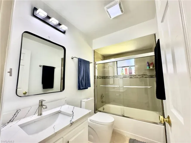 Full bath featuring vanity, toilet, bath / shower combo with glass door, and tile patterned flooring