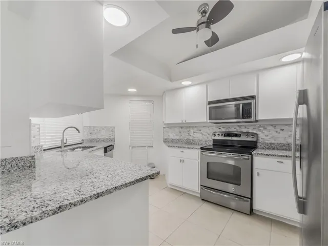 Kitchen with appliances with stainless steel finishes, a sink, a ceiling fan, decorative backsplash, and light stone countertops
