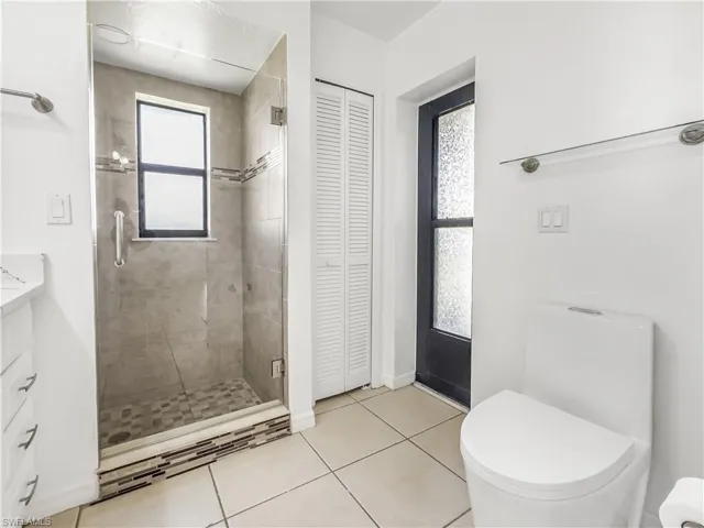 Bathroom with a closet, toilet, vanity, a stall shower, and tile patterned flooring