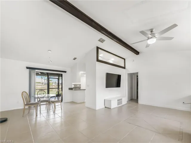 Unfurnished living room featuring beam ceiling, light tile patterned floors, ceiling fan, high vaulted ceiling, and baseboards