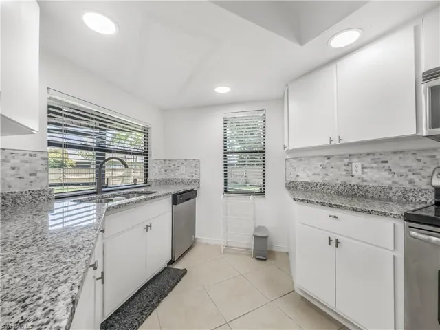 Kitchen featuring dishwasher, range, a sink, decorative backsplash, and white cabinetry