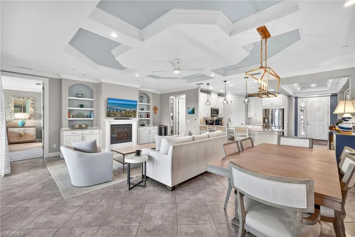 Living area featuring ornamental molding, a glass covered fireplace, coffered ceiling, a chandelier, and light tile patterned floors