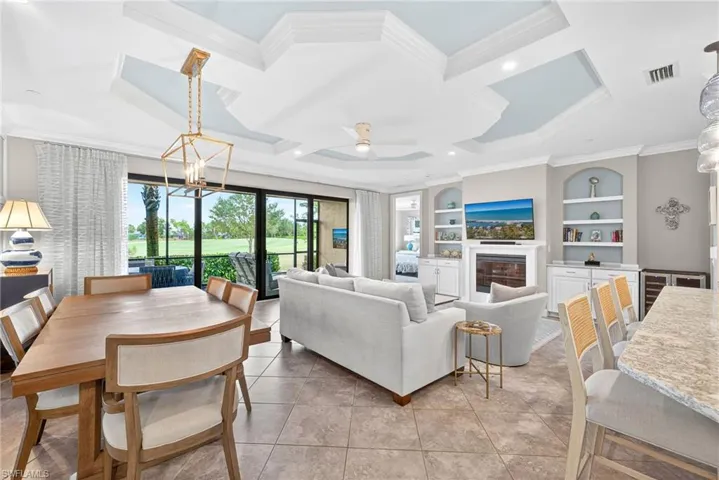 Living area featuring crown molding, a glass covered fireplace, built in shelves, coffered ceiling, and a chandelier