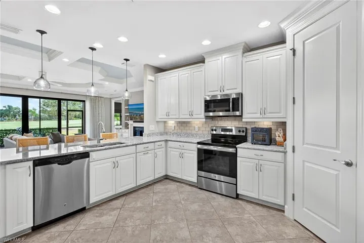 Kitchen with stainless steel appliances, white cabinets, light stone counters, decorative backsplash, and recessed lighting
