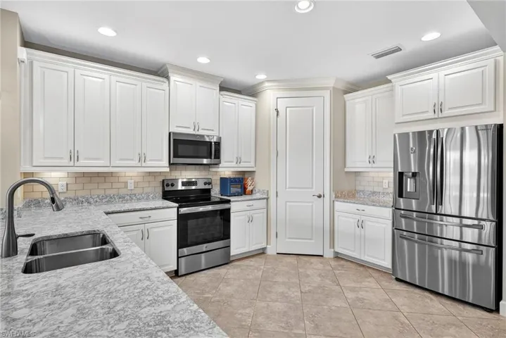 Kitchen with stainless steel appliances, light stone countertops, white cabinets, recessed lighting, and light tile patterned flooring