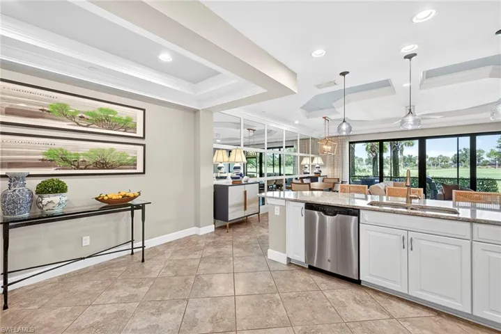 Kitchen featuring white cabinets, light stone countertops, pendant lighting, stainless steel dishwasher, and ornamental molding