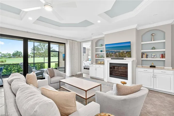 Living area featuring a glass covered fireplace, light tile patterned flooring, ornamental molding, recessed lighting, and coffered ceiling