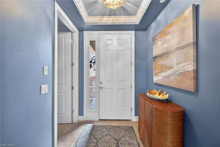Entrance foyer featuring a tray ceiling, crown molding, tile patterned floors, a chandelier, and a textured wall