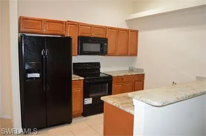 Kitchen featuring black appliances, wood finish cabinets, a peninsula, and light tile patterned flooring
