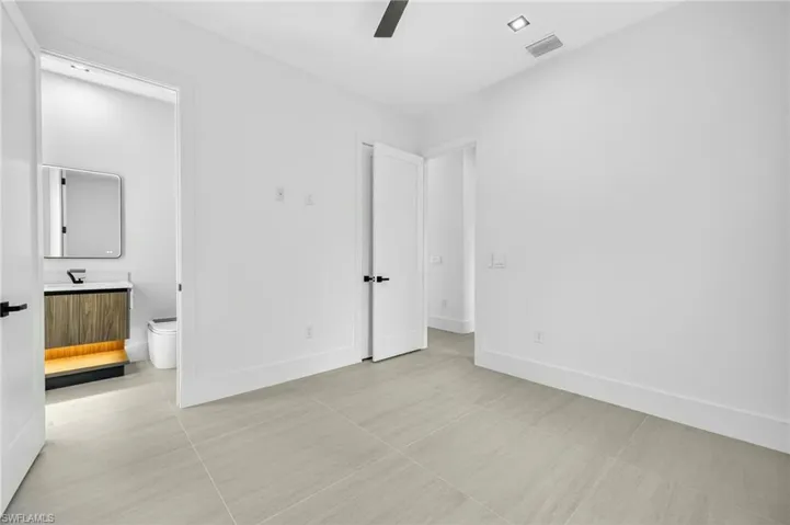 Unfurnished bedroom featuring connected bathroom, light tile patterned floors, and a ceiling fan
