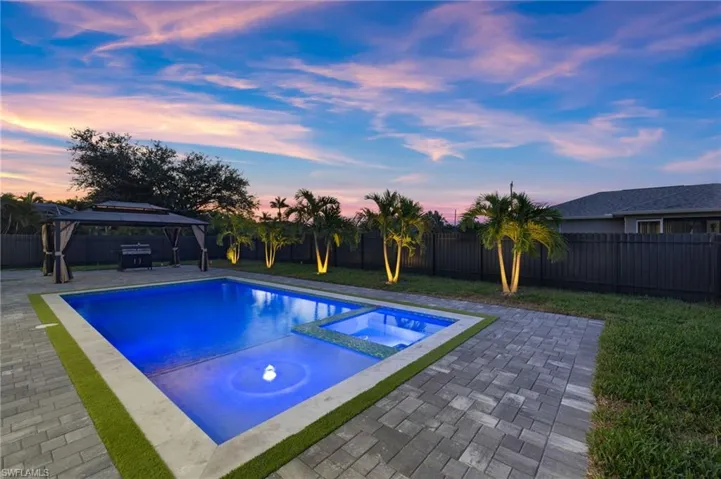 Pool at dusk featuring a gazebo, a pool with connected hot tub, a patio, and a fenced backyard