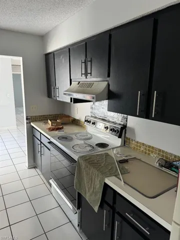 Kitchen with white electric range, tasteful backsplash, custom exhaust hood, a textured ceiling, and light tile floors