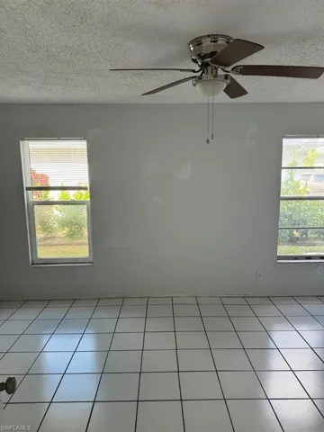 Tiled empty room featuring ceiling fan and a textured ceiling