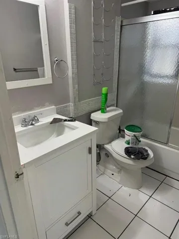 Full bathroom featuring shower / bath combination with glass door, tile flooring, vanity, and toilet