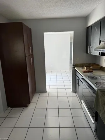 Kitchen with white electric stove, a textured ceiling, light tile floors, and premium range hood