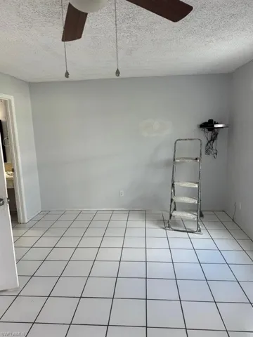 Tiled empty room with ceiling fan and a textured ceiling