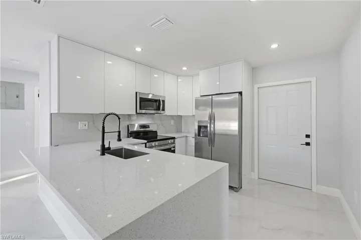 Kitchen featuring modern cabinets, stainless steel appliances, white cabinets, a peninsula, and light stone countertops