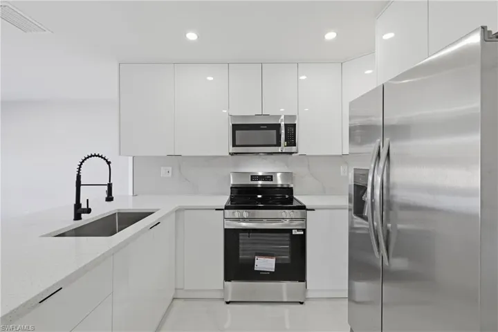 Kitchen featuring stainless steel appliances, white cabinets, modern cabinets, light stone countertops, and recessed lighting