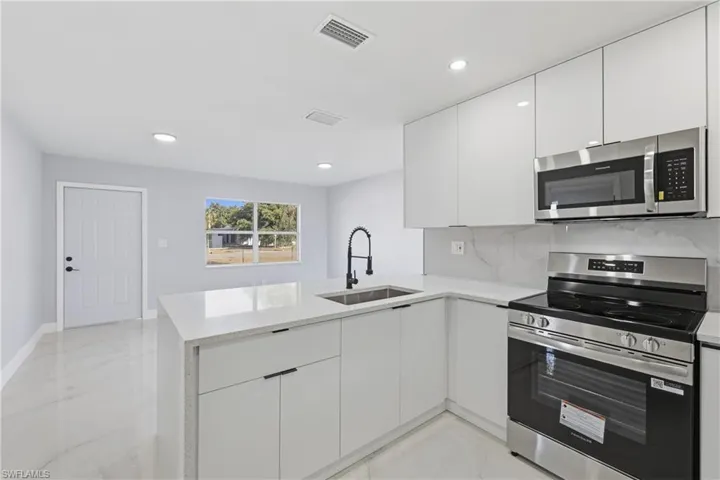 Kitchen with appliances with stainless steel finishes, modern cabinets, white cabinets, a peninsula, and backsplash