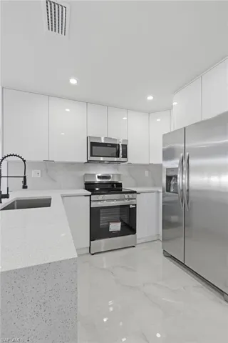 Kitchen featuring modern cabinets, white cabinets, appliances with stainless steel finishes, light stone counters, and decorative backsplash