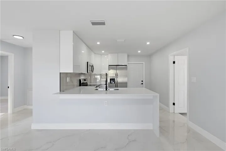 Kitchen featuring modern cabinets, white cabinets, appliances with stainless steel finishes, a peninsula, and light stone counters