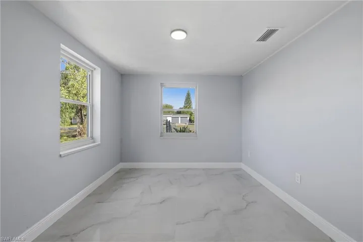 Unfurnished room featuring light marble finish flooring and baseboards