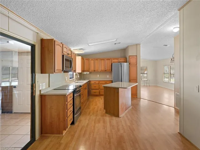 Kitchen featuring stainless steel appliances, a center island, light wood-style flooring, light countertops, and vaulted ceiling