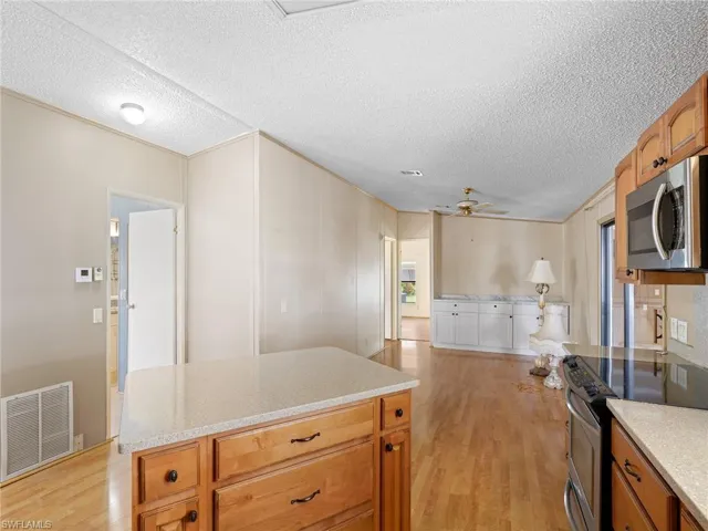 Kitchen featuring appliances with stainless steel finishes, light wood-style floors, brown cabinetry, a textured ceiling, and open floor plan