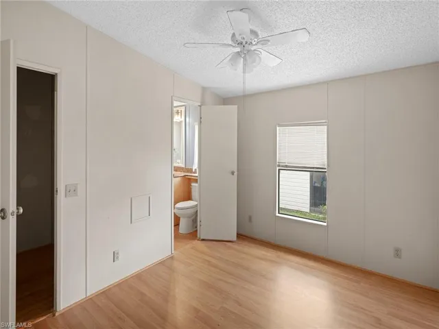Unfurnished bedroom featuring light wood-style flooring, a decorative wall, a textured ceiling, and connected bathroom