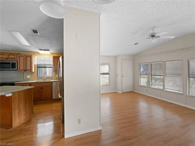 Kitchen with brown cabinets, light wood-style flooring, a ceiling fan, a textured ceiling, and appliances with stainless steel finishes